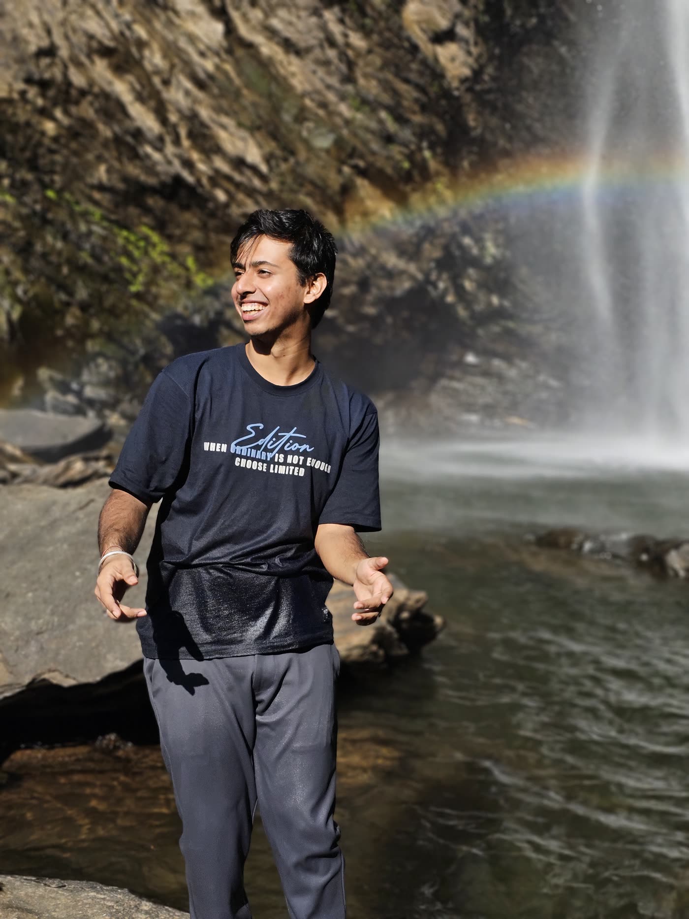 Aryan laughing, soaked, in front of Kudlu Theertha Falls with a rainbow across the spray